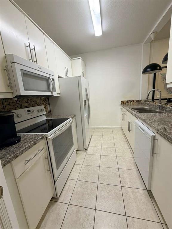 A galley kitchen features white cabinets, stainless steel appliances, and a tiled backsplash — 6214 STEVENSON DRIVE UNIT 303, ORLANDO, FL