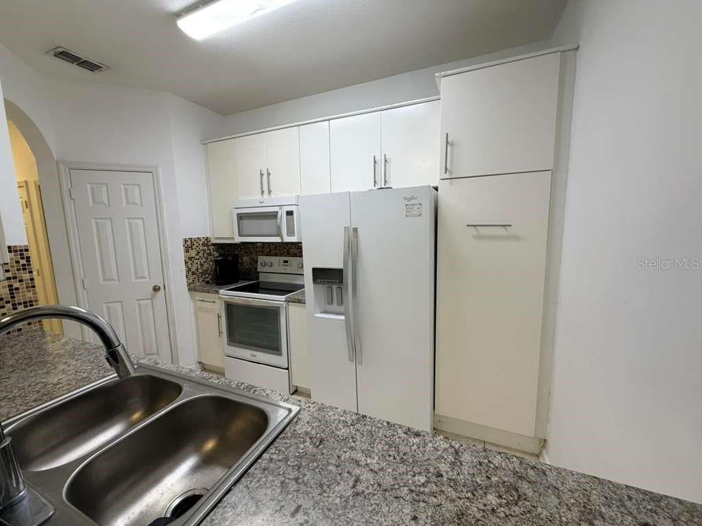 A kitchen features white cabinetry, a white refrigerator, a white stove, and granite countertops — 6214 STEVENSON DRIVE UNIT 303, ORLANDO, FL