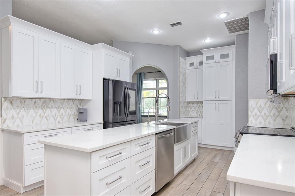 A modern kitchen features white cabinetry, quartz countertops, stainless steel appliances, and a tiled backsplash — 10537 VERSAILLES BOULEVARD, CLERMONT, FL