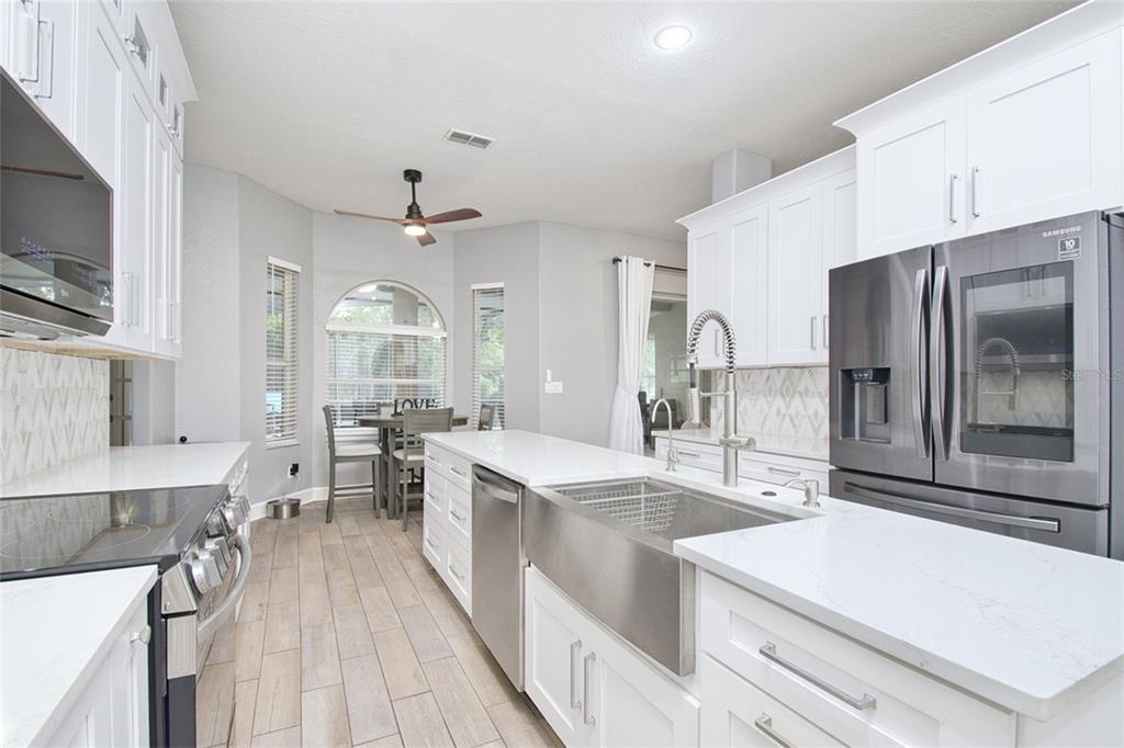 A modern kitchen features white cabinetry, quartz countertops, stainless steel appliances, and wood-look tile flooring — 10537 VERSAILLES BOULEVARD, CLERMONT, FL