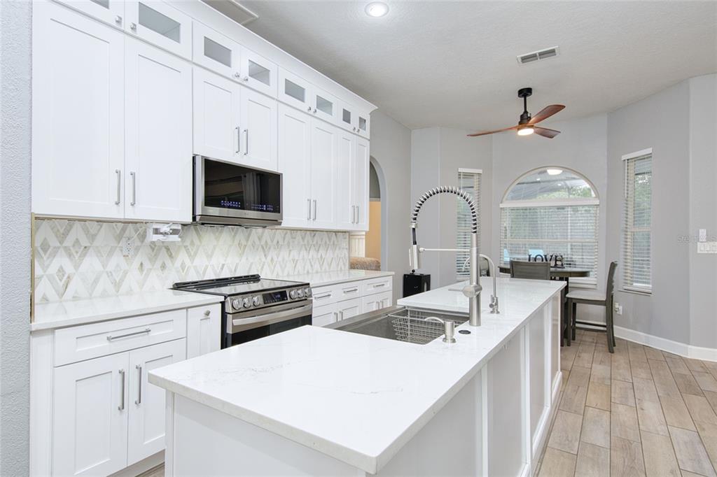 A modern kitchen features white cabinetry, quartz countertops, a large island, and stainless steel appliances — 10537 VERSAILLES BOULEVARD, CLERMONT, FL