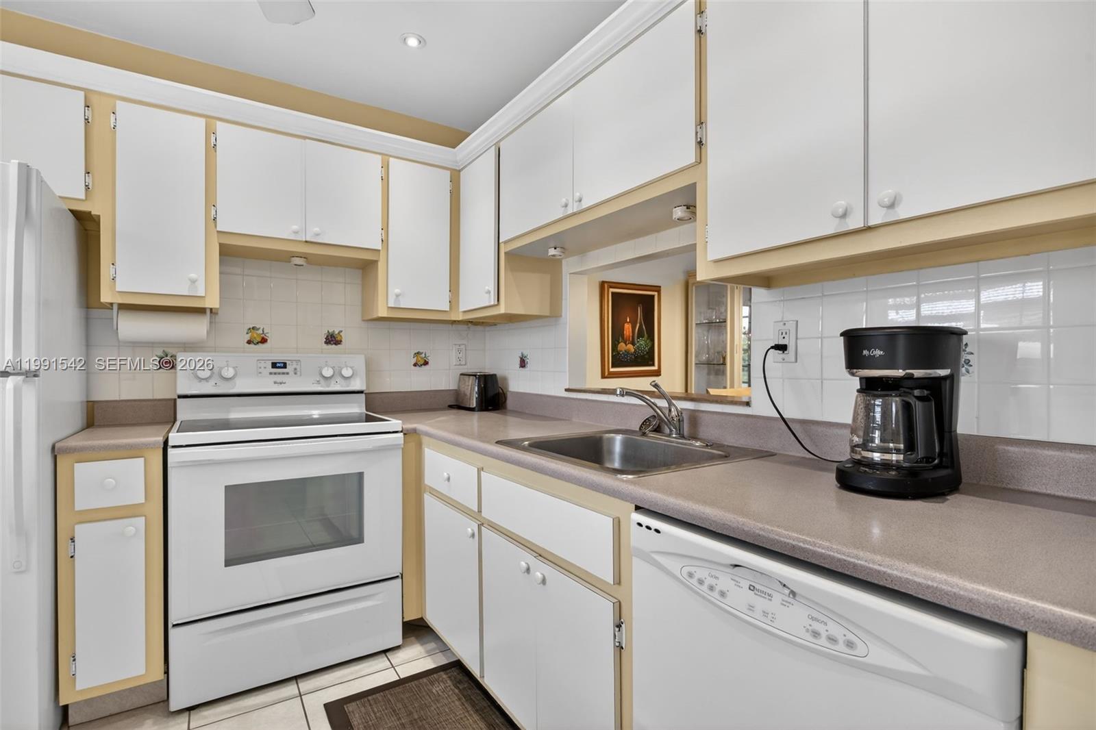 A kitchen features white cabinets with yellow trim, a white range, and a stainless sink — 4299 NW 16th St # 202, Lauderhill FL 33313, LAUDERHILL, FL