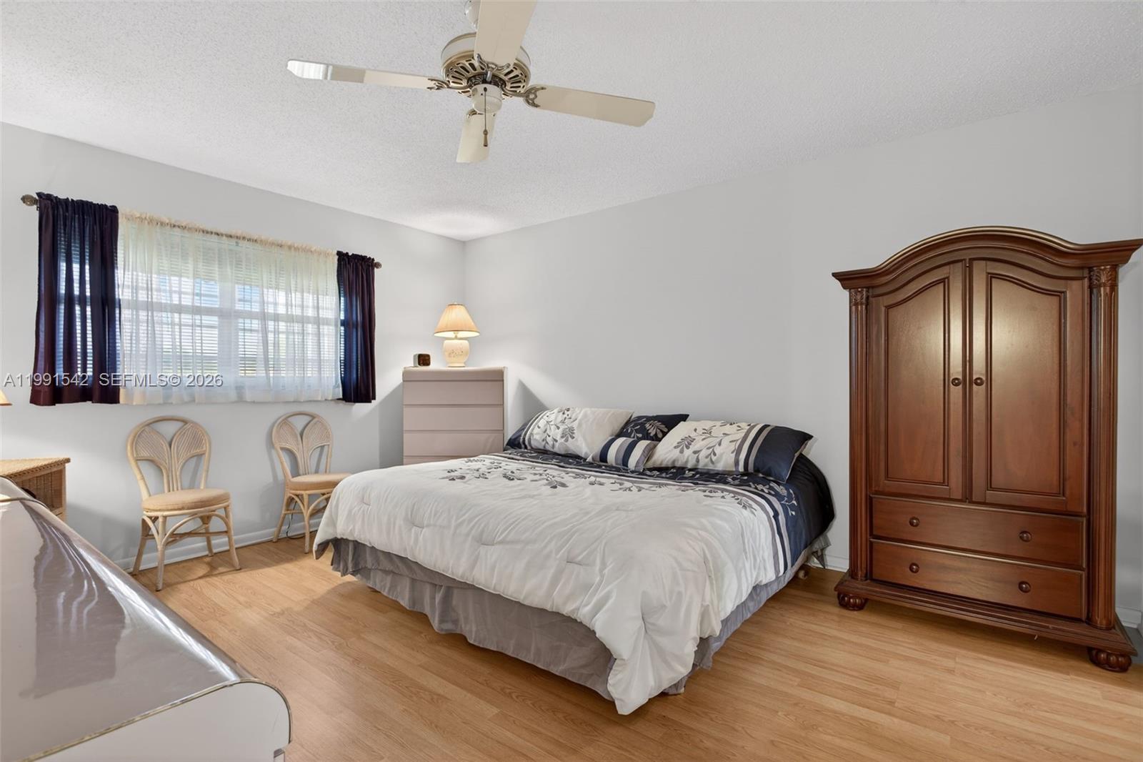 A bedroom features a bed, a large wooden armoire, two wicker chairs, and wood flooring — 4299 NW 16th St # 202, Lauderhill FL 33313, LAUDERHILL, FL