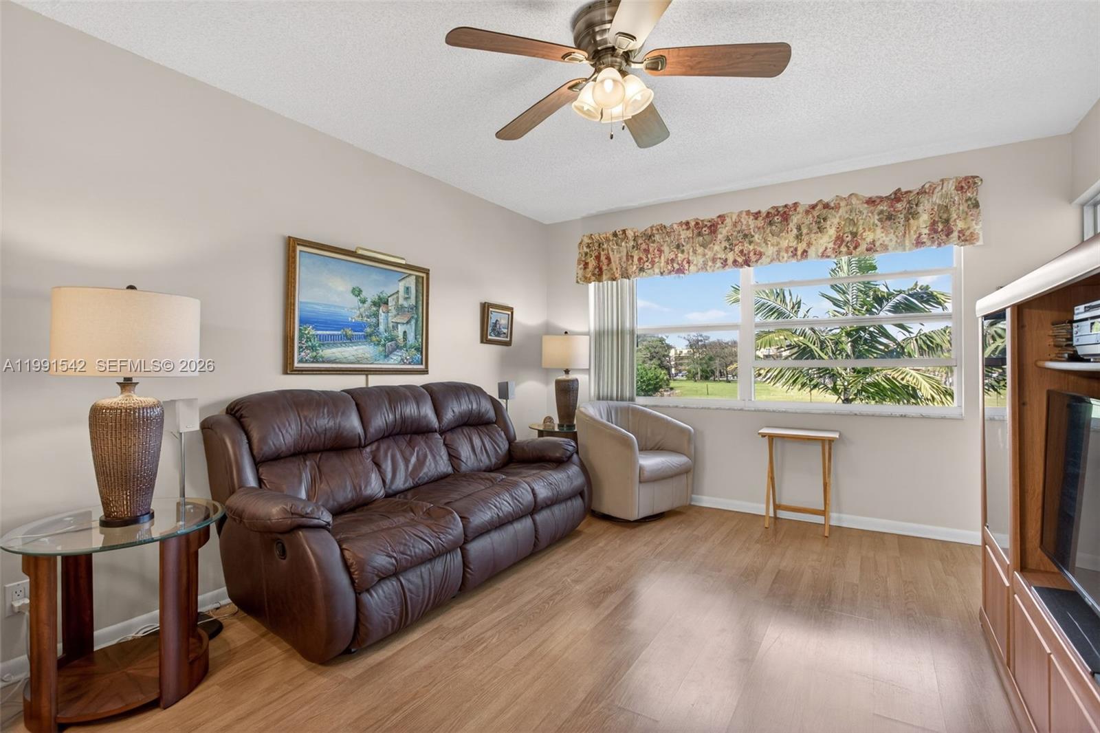A living room features a brown leather sofa, wood flooring, a ceiling fan, and windows — 4299 NW 16th St # 202, Lauderhill FL 33313, LAUDERHILL, FL
