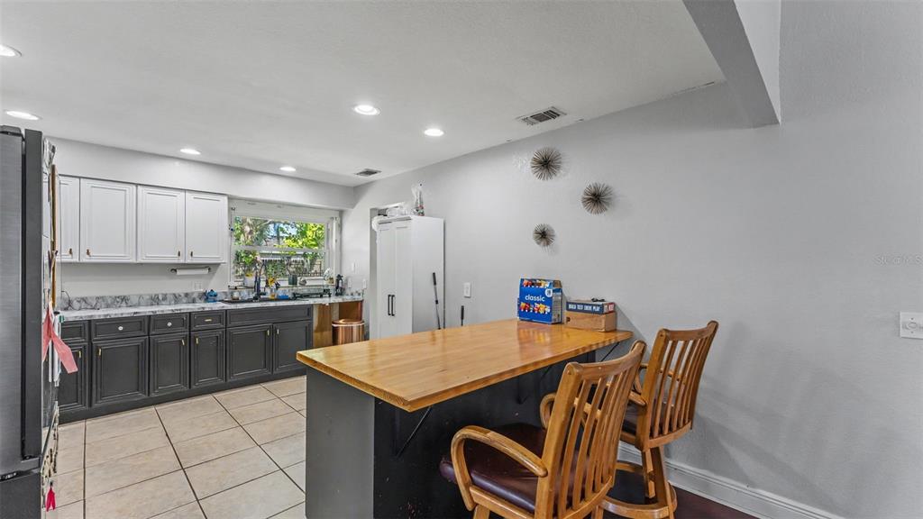 A kitchen features two-toned cabinets, a wooden island with bar stools, and tiled flooring — 5060 STARLING DRIVE, MULBERRY, FL