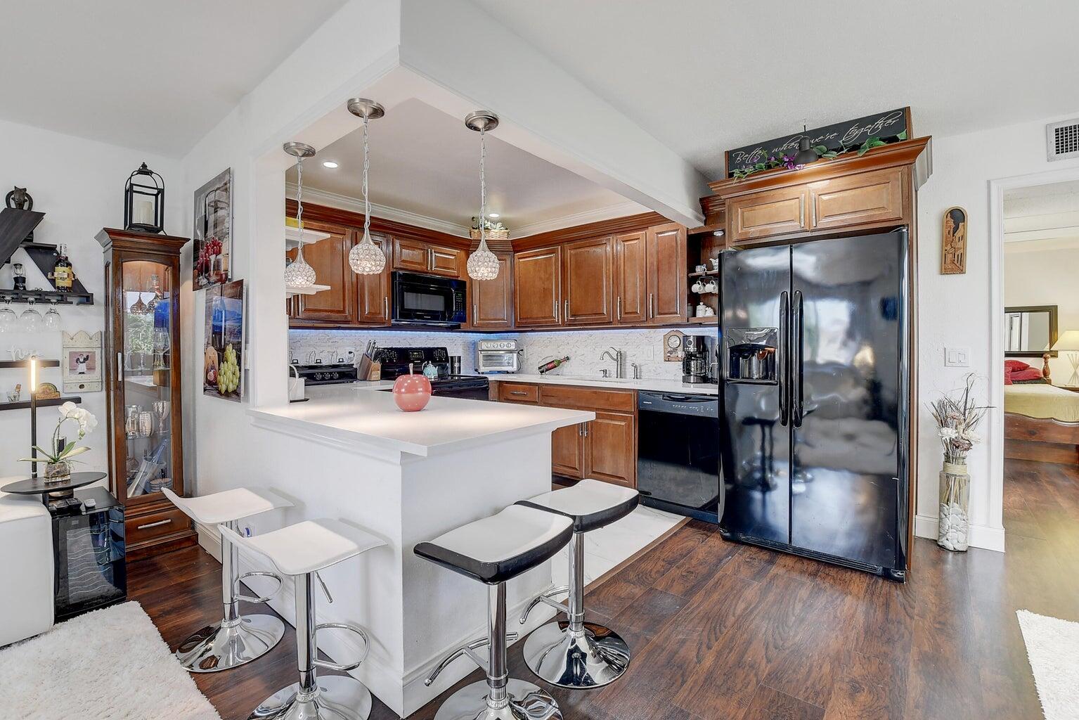 A kitchen features wood cabinets, a white breakfast bar with stools, and black appliances — 123 Saxony C, Delray Beach FL 33446, DELRAY BEACH, FL