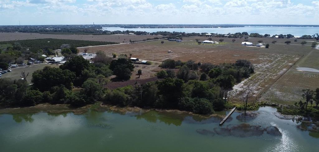 An aerial view shows a large grassy field, wooded areas, and a dock on a lake — 100 CLOVERLEAF ROAD, LAKE PLACID, FL