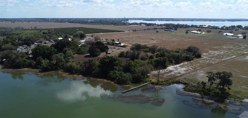 An aerial view shows a waterfront property with a wooden dock and surrounding rural land — 100 CLOVERLEAF ROAD, LAKE PLACID, FL