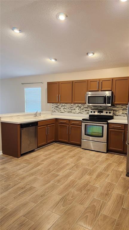 A kitchen features brown cabinets, stainless steel appliances, a tiled backsplash, and wood-look flooring — 7955 CARRIAGE POINTE DRIVE, GIBSONTON, FL