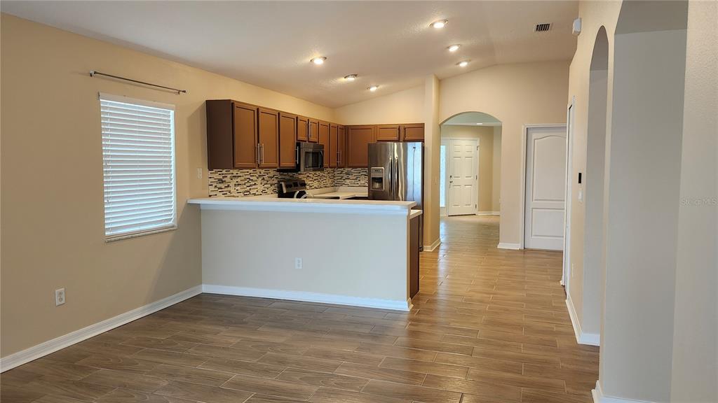 A kitchen with wood cabinets and stainless steel appliances overlooks a dining area with tile floors — 7955 CARRIAGE POINTE DRIVE, GIBSONTON, FL