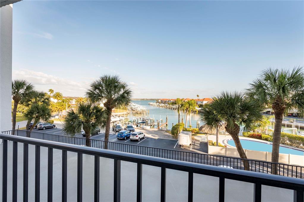 A balcony view overlooking a parking lot, a marina with boats, and a swimming pool — 1591 GULF BOULEVARD UNIT 203S, CLEARWATER BEACH, FL