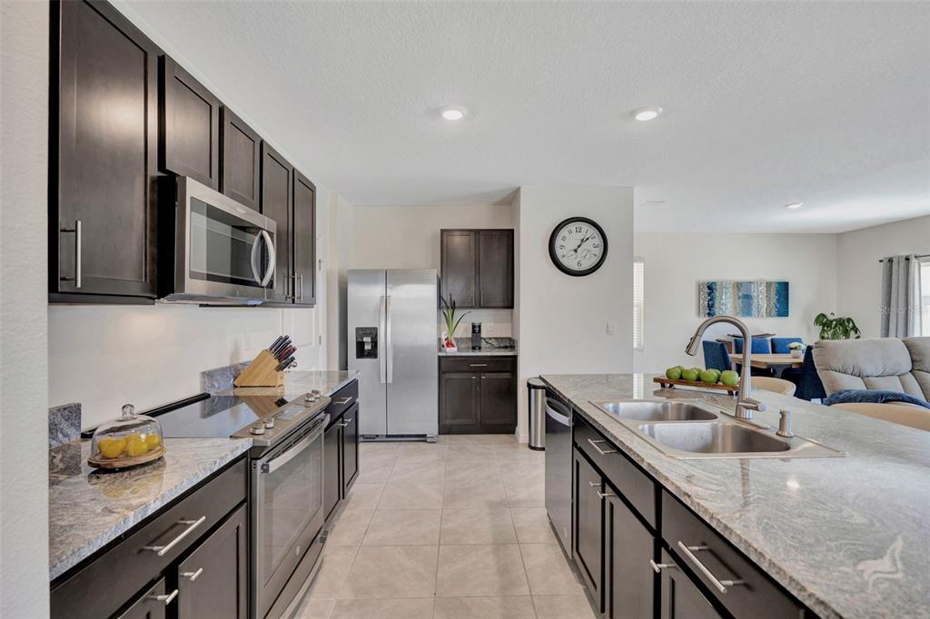 A modern kitchen features dark wood cabinets, stainless steel appliances, and a granite-topped island — 5758 HOLLINGWORTH TRAIL, WESLEY CHAPEL, FL