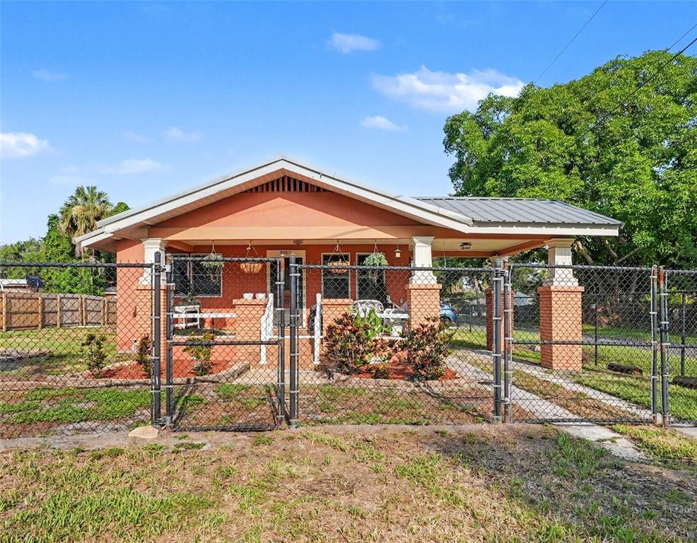 A single-story orange house with a front porch sits behind a chain-link fence — 9907 MAGGIE STREET, GIBSONTON, FL