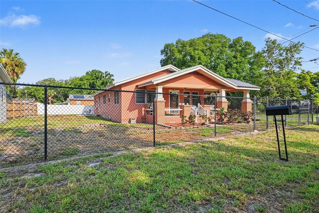 A single-story orange house with a front porch is enclosed by a chain-link fence — 9907 MAGGIE STREET, GIBSONTON, FL