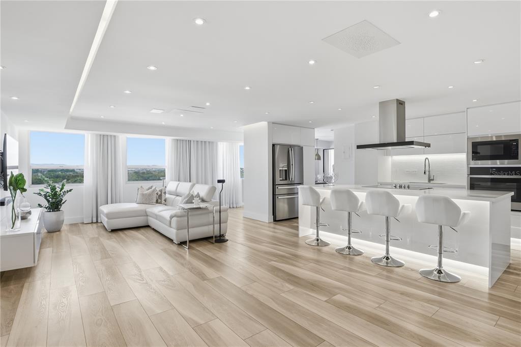 A modern open-concept kitchen and living area features white cabinetry, bar seating, and wood flooring — 3307 ISLA VERDE AVE. UNIT 1, CAROLINA, PR