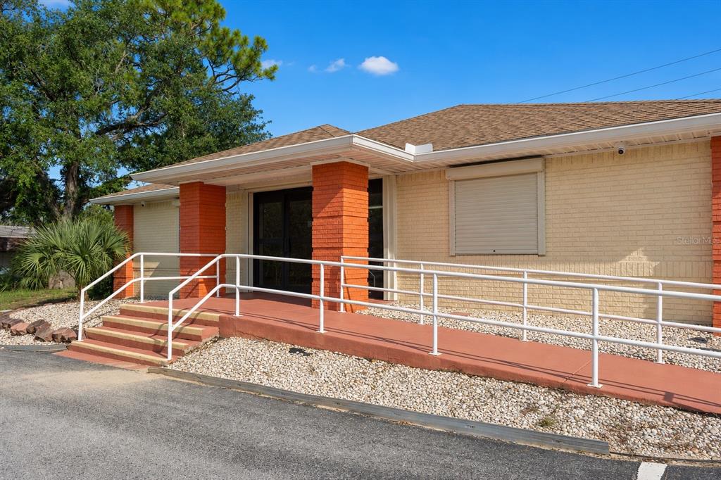 A single-story brick building features a wheelchair ramp, stairs, and orange-painted support columns — 10507 SPRING HILL DRIVE, SPRING HILL, FL