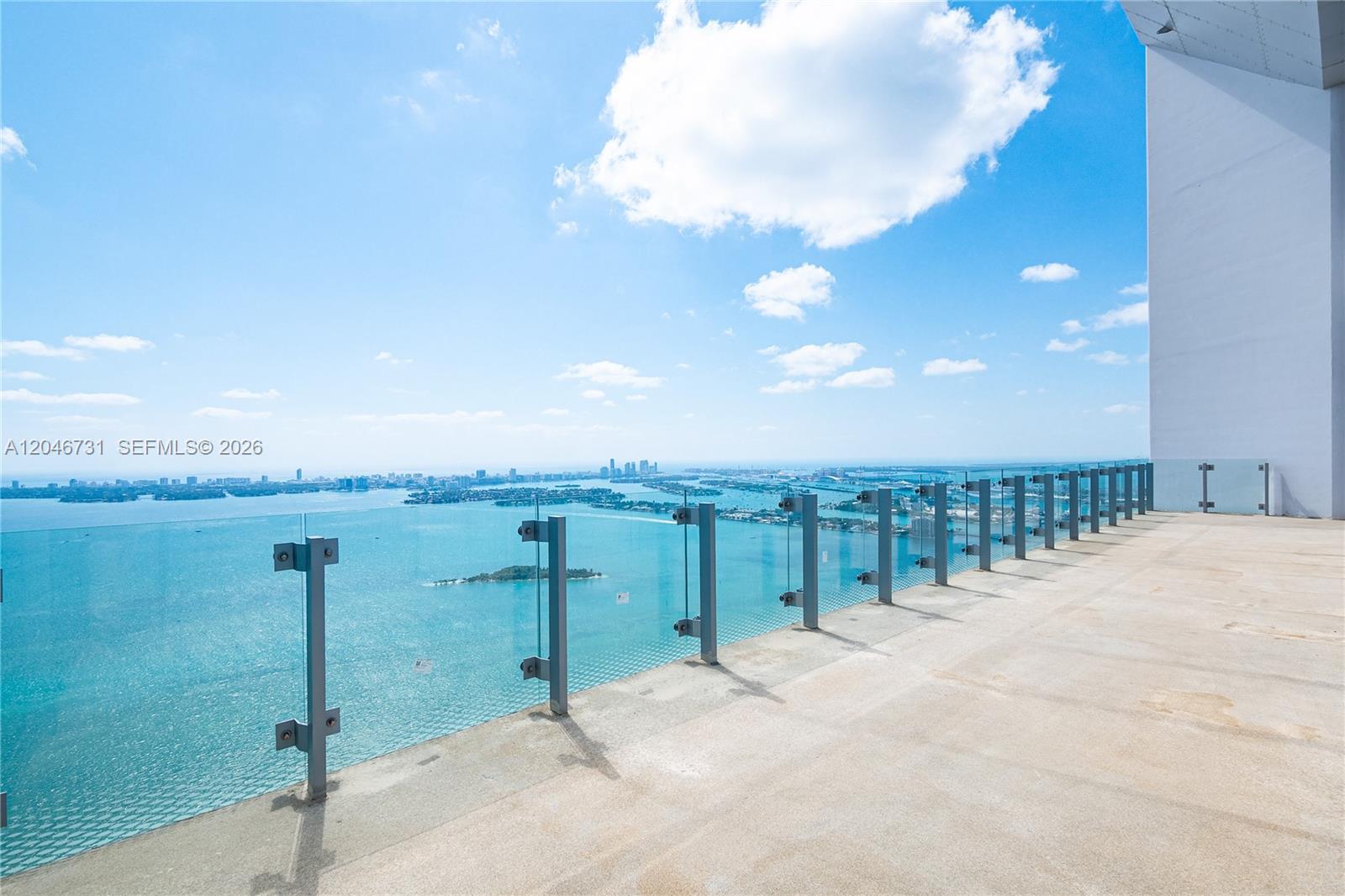 A high-rise balcony features a glass railing overlooking a bay and city skyline — 700 NE 26th Ter # 02, Miami FL 33137, MIAMI, FL