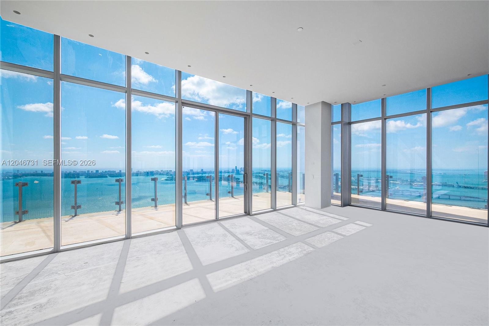 An empty room with floor-to-ceiling windows, concrete flooring, and a balcony overlooking the ocean — 700 NE 26th Ter # 02, Miami FL 33137, MIAMI, FL