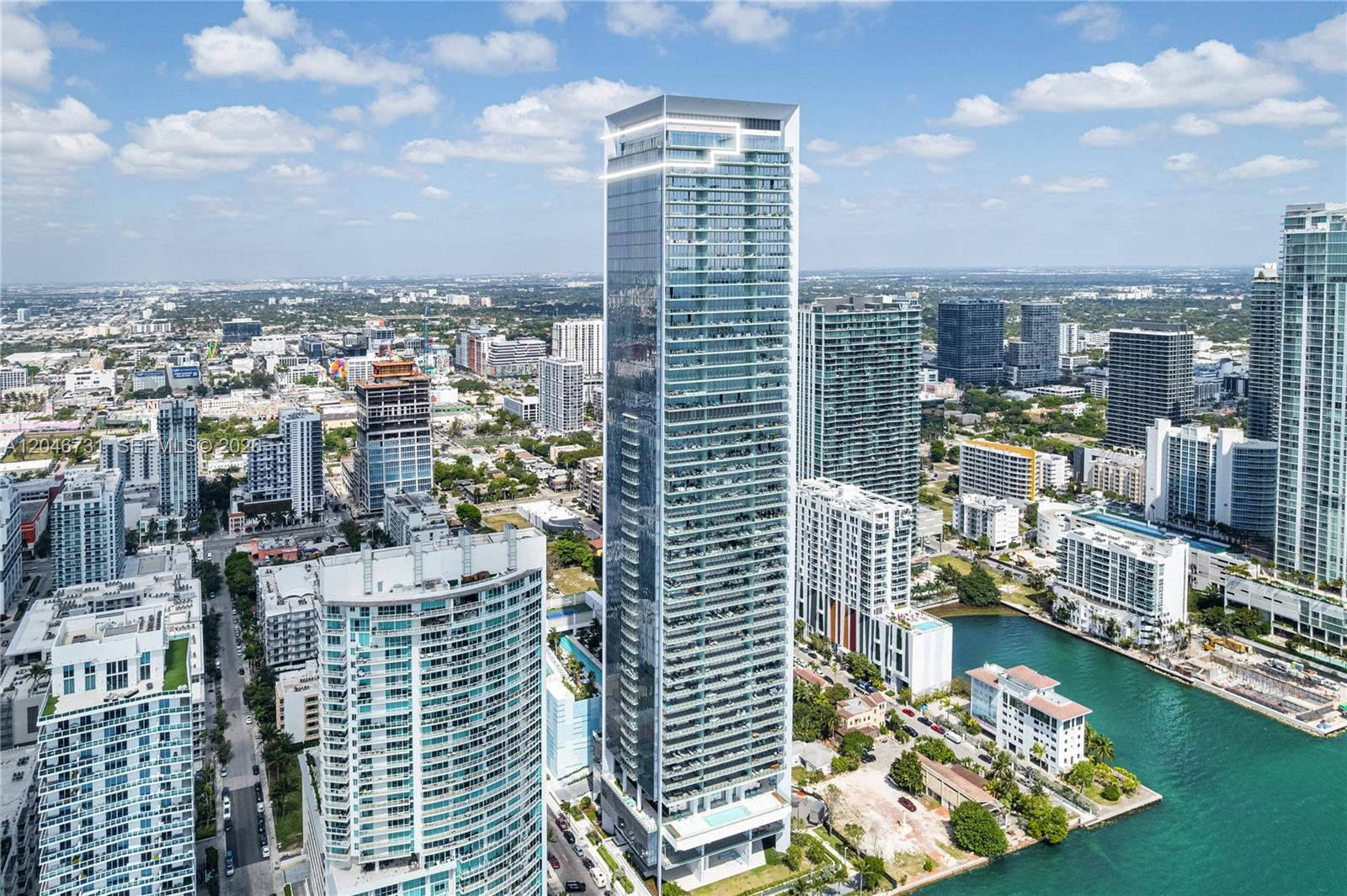 An aerial view of a tall, modern glass skyscraper surrounded by other urban high-rise buildings — 700 NE 26th Ter # 02, Miami FL 33137, MIAMI, FL