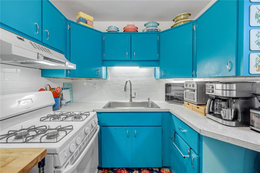 A kitchen features bright blue cabinets, a white gas stove, and a stainless steel sink — 2805 SAXON DRIVE, NEW SMYRNA BEACH, FL