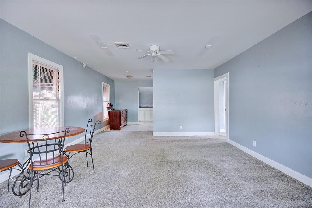 A room with light blue walls, gray carpeting, a ceiling fan, and a small dining set — 121 BATES AVENUE SE, WINTER HAVEN, FL