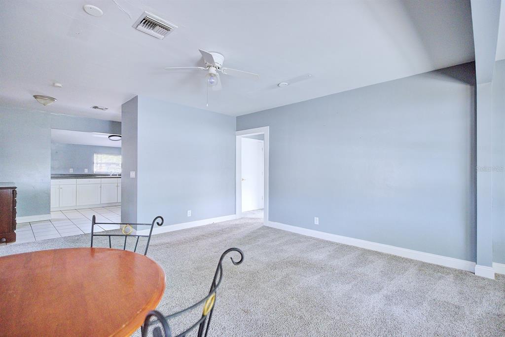A carpeted living room with light blue walls, a ceiling fan, and an adjacent kitchen — 121 BATES AVENUE SE, WINTER HAVEN, FL