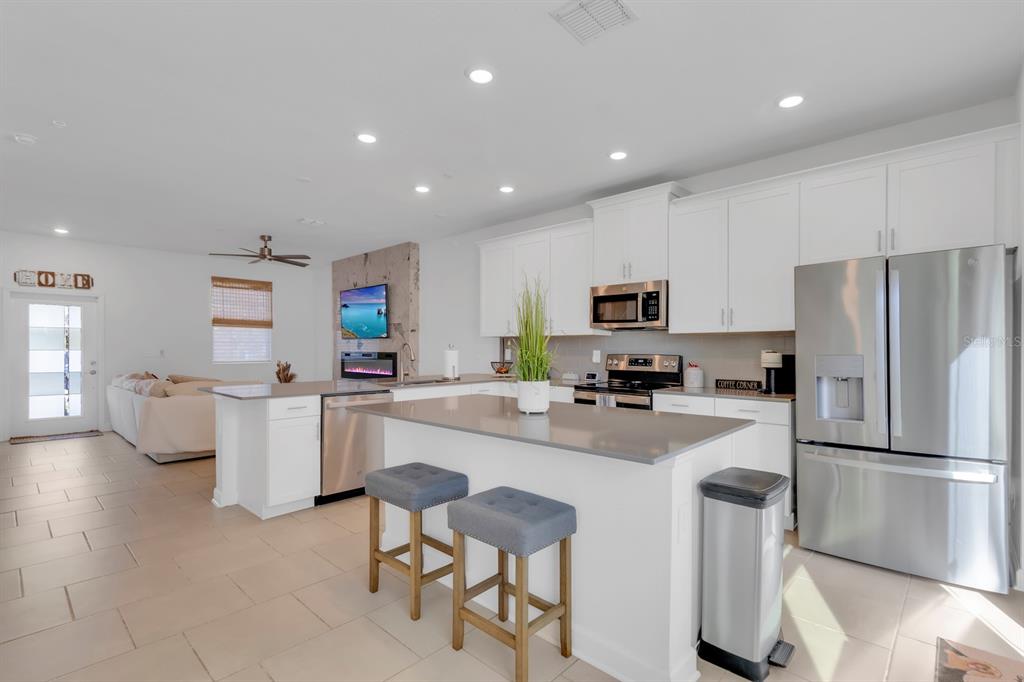 A modern kitchen features white cabinetry, stainless steel appliances, a gray island, and bar stools — 11245 LISTENING DRIVE, ORLANDO, FL