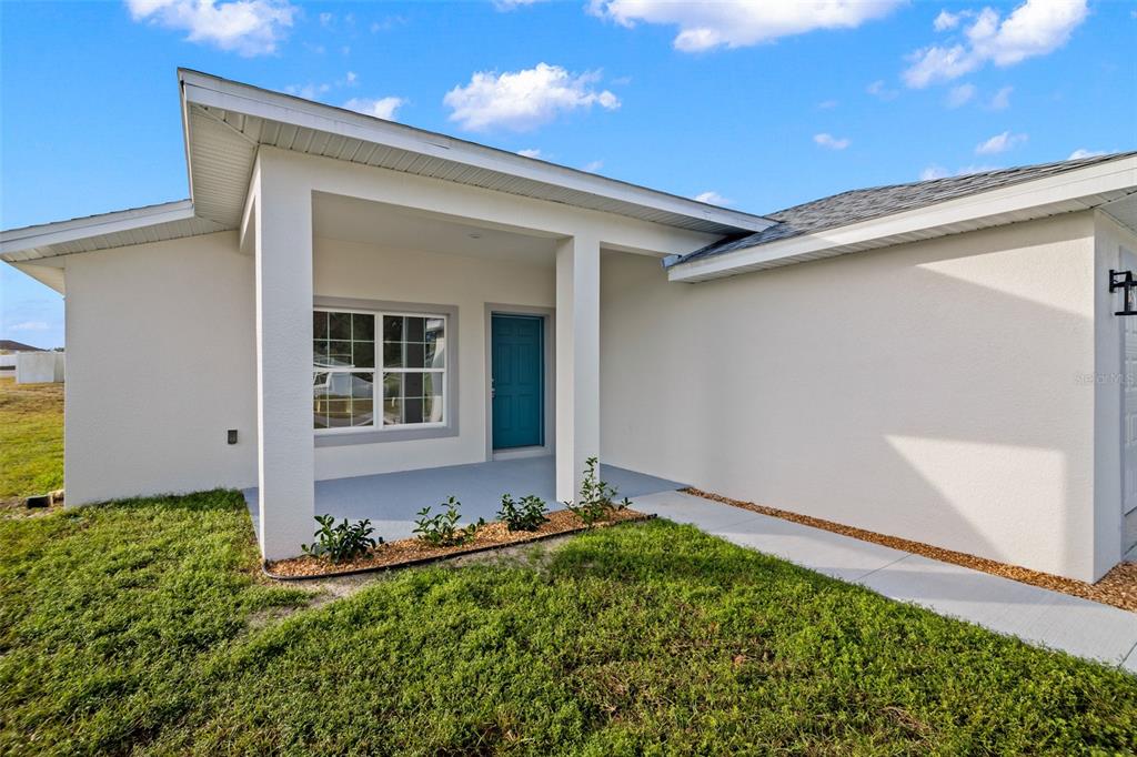 The exterior of a single-story house features a covered entryway, a teal door, and landscaping — 5346 SE 91ST STREET, OCALA, FL
