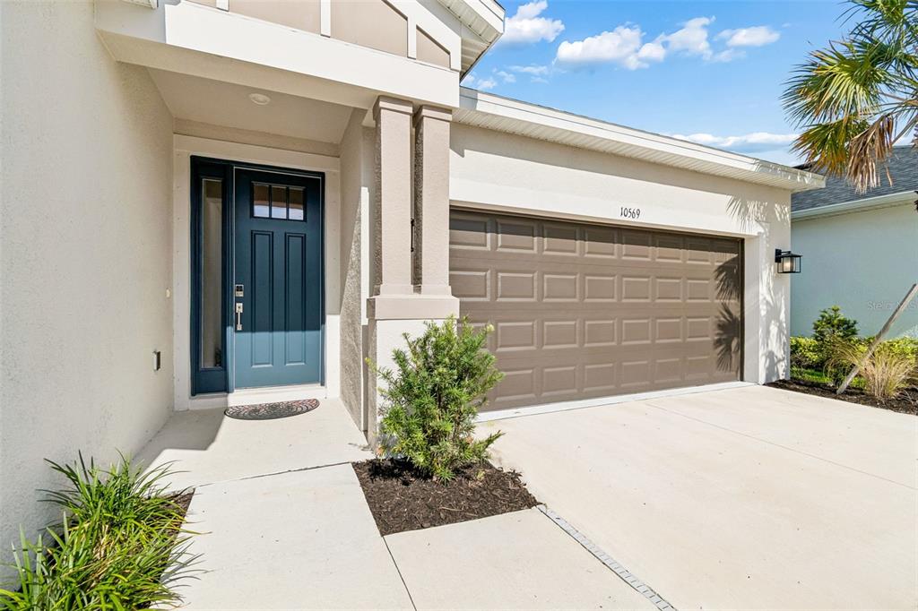 The exterior of a house features a blue front door and a two-car garage — 10569 TRANQUIL MEADOW LOOP, RIVERVIEW, FL