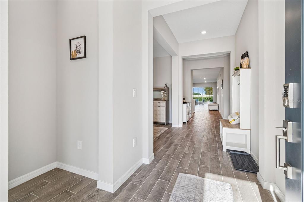 A bright entryway features wood-look tile flooring, a white hall tree, and a view through — 10569 TRANQUIL MEADOW LOOP, RIVERVIEW, FL