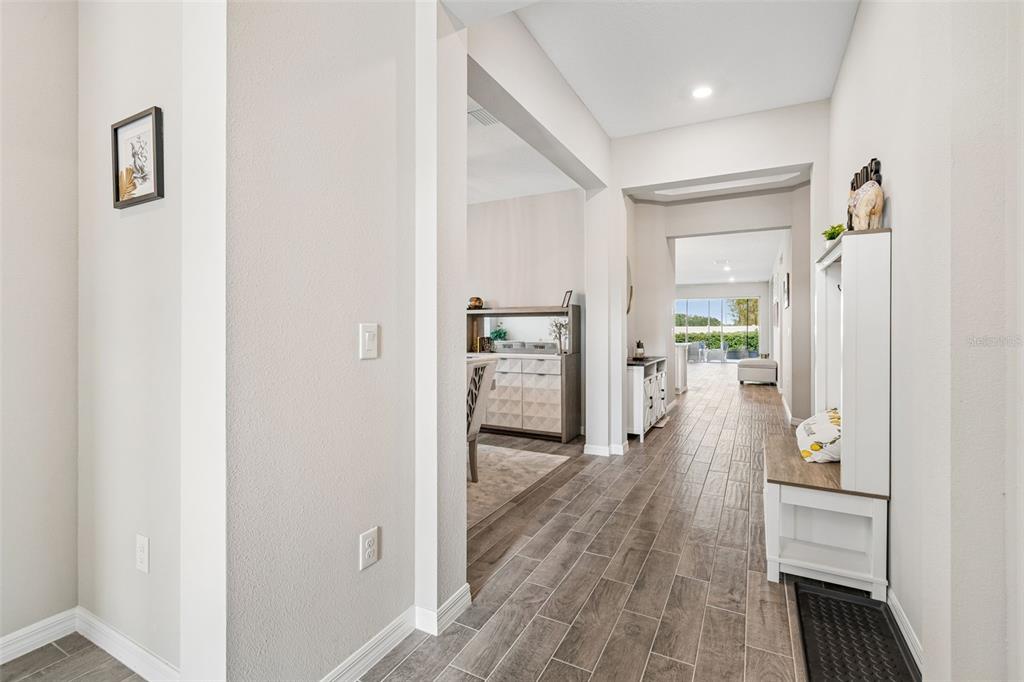 A hallway with wood-look tile flooring leads to an open dining area and living space — 10569 TRANQUIL MEADOW LOOP, RIVERVIEW, FL