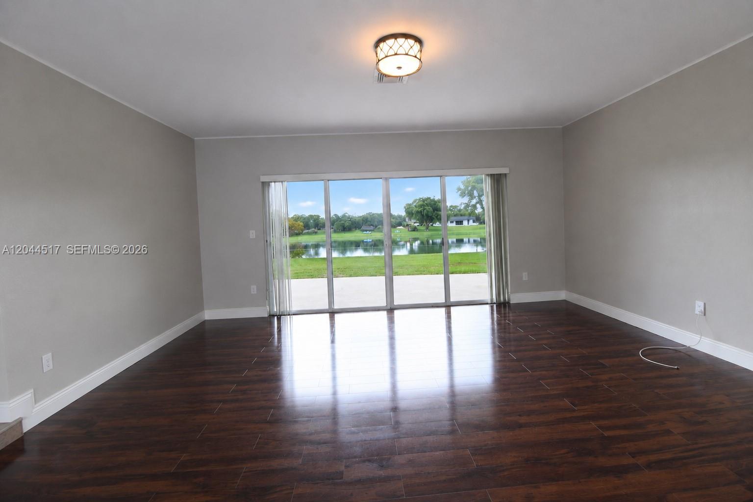 An empty room features dark wood flooring, light gray walls, and large sliding glass doors — 15445 SW 99th Ave # 15445, Miami FL 33157, MIAMI, FL