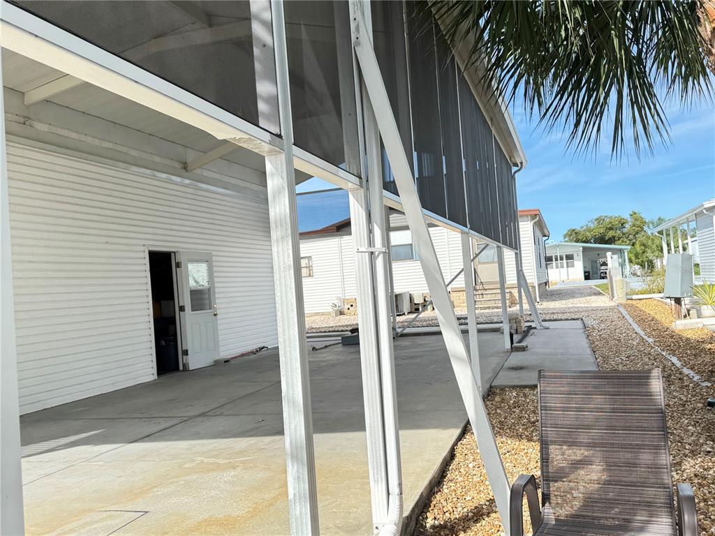 A covered concrete patio area features white siding, screen walls, and a metal support beam — 35103 JADE DRIVE, ZEPHYRHILLS, FL