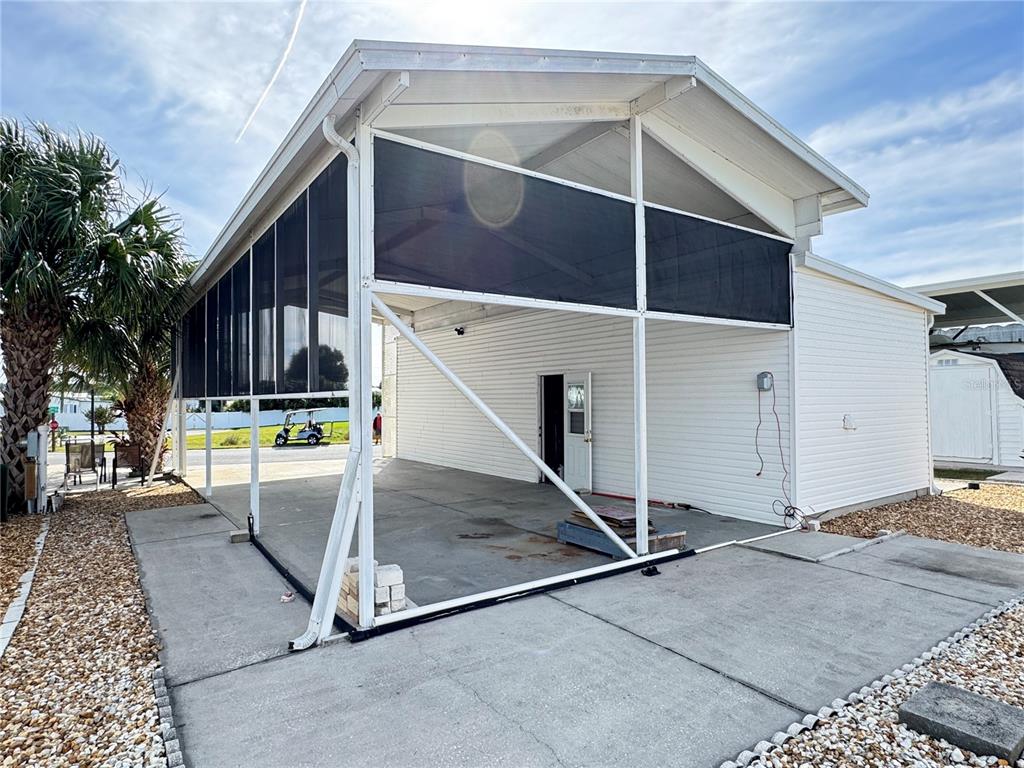 A white-sided structure features a large, open-air concrete patio enclosed by black privacy screens — 35103 JADE DRIVE, ZEPHYRHILLS, FL