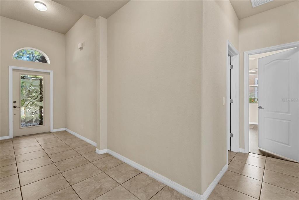 An entryway features beige tile flooring, a front door with a decorative glass insert, and walls — 11711 BREADFRUIT LANE, VENICE, FL