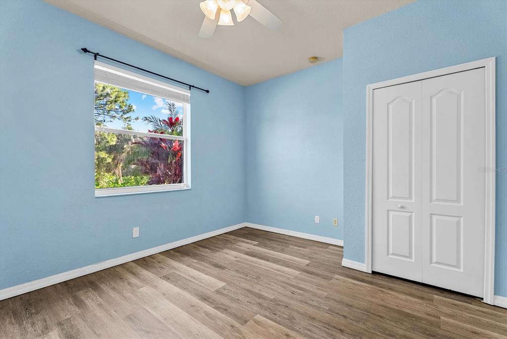 A bedroom with light blue walls, wood-look flooring, a ceiling fan, and a white closet — 11711 BREADFRUIT LANE, VENICE, FL