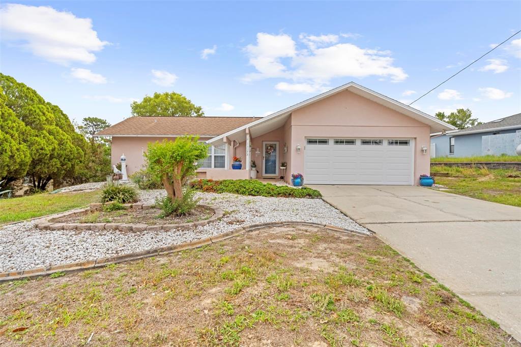 A single-story house with a pink exterior, a two-car garage, and a gravel front yard — 13378 DRAYTON DRIVE, SPRING HILL, FL