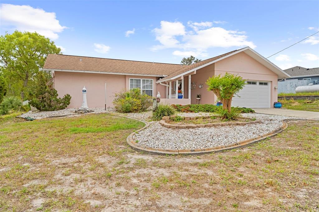 A single-story pink house features a gravel front yard, a tree, and a garage — 13378 DRAYTON DRIVE, SPRING HILL, FL