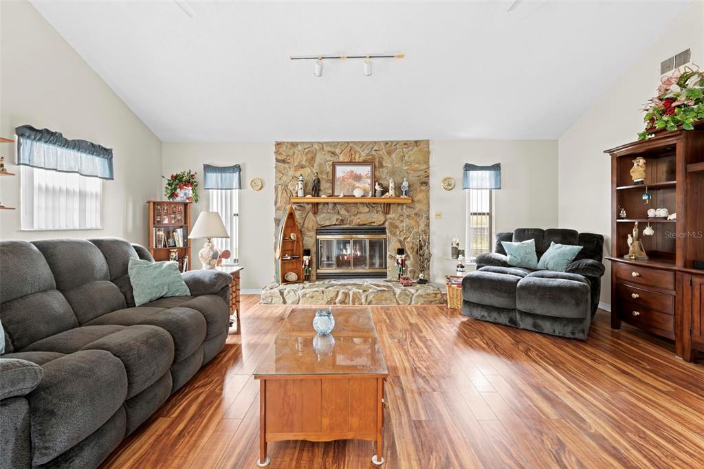 A living room features a stone fireplace, wood-look flooring, and dark gray upholstered furniture — 13378 DRAYTON DRIVE, SPRING HILL, FL