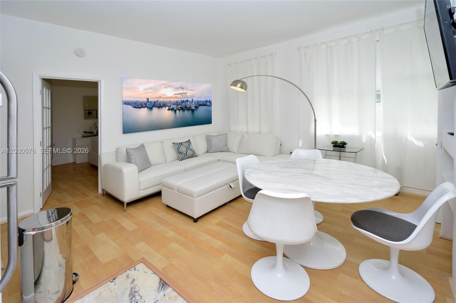 A living and dining area features a white sectional sofa, marble table, and hardwood floors — 1342 Drexel Ave # 105, Miami Beach FL 33139, MIAMI BEACH, FL