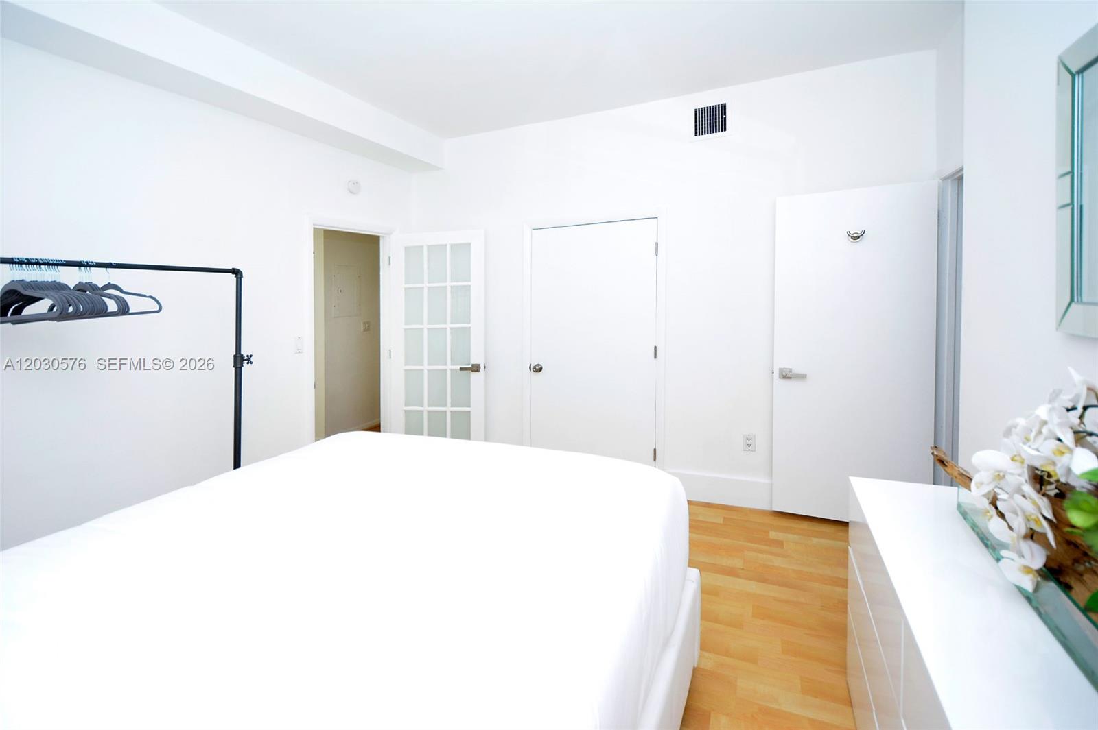 A bedroom with white walls, light wood flooring, a bed, and multiple interior doors — 1342 Drexel Ave # 105, Miami Beach FL 33139, MIAMI BEACH, FL