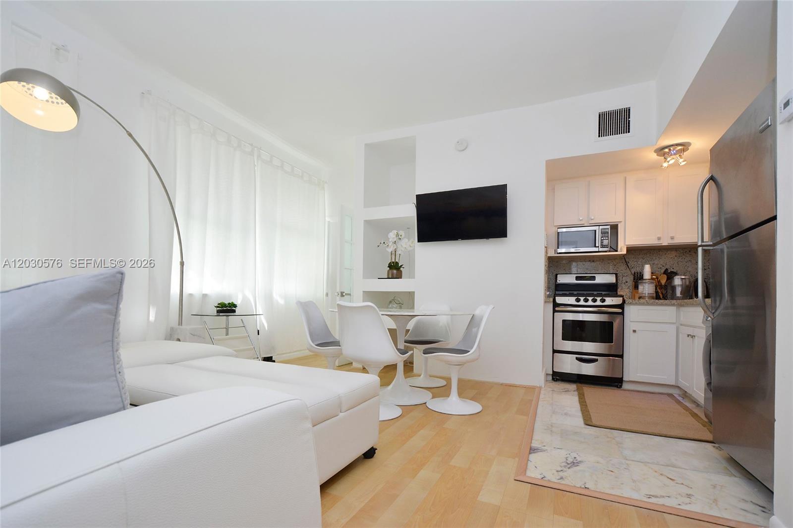 A small, open-concept living and dining area features white furniture, hardwood floors, and a kitchen — 1342 Drexel Ave # 105, Miami Beach FL 33139, MIAMI BEACH, FL