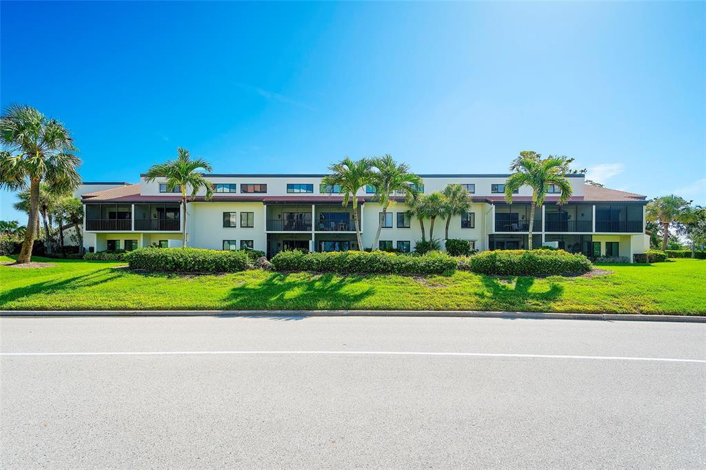 A two-story residential building with screened balconies sits behind a manicured lawn and palm trees — 2039 GULF OF MEXICO DRIVE UNIT G3-207, LONGBOAT KEY, FL