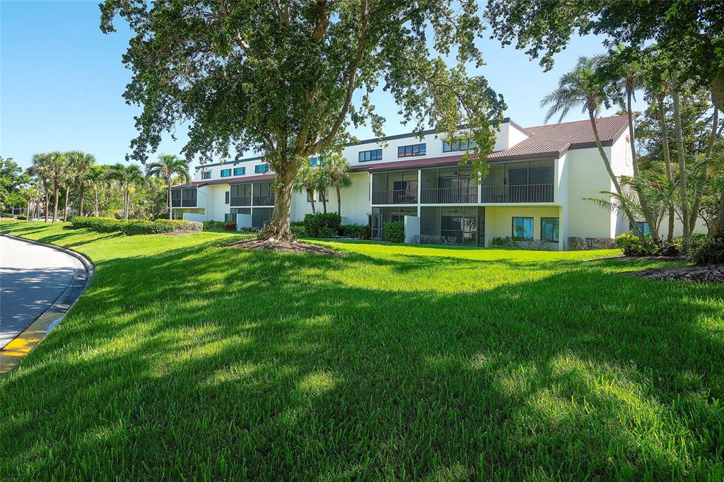 A multi-story apartment building with screened balconies sits behind a large tree and lawn — 2039 GULF OF MEXICO DRIVE UNIT G3-207, LONGBOAT KEY, FL