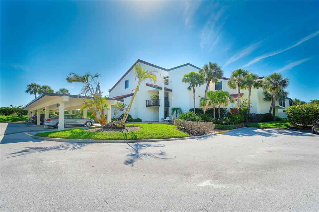 A multi-story apartment building with a covered parking area and palm trees under a blue sky — 2039 GULF OF MEXICO DRIVE UNIT G3-207, LONGBOAT KEY, FL