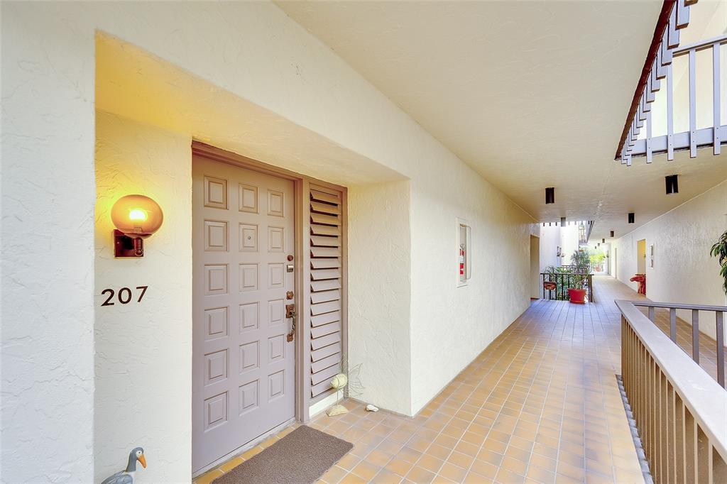 An exterior view of a residential unit entrance with a numbered door and tiled walkway — 2039 GULF OF MEXICO DRIVE UNIT G3-207, LONGBOAT KEY, FL