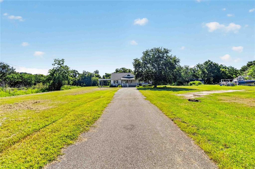 A long asphalt driveway leads to a single-story house surrounded by a large grassy yard — 2994 BIG SKY BOULEVARD, KISSIMMEE, FL