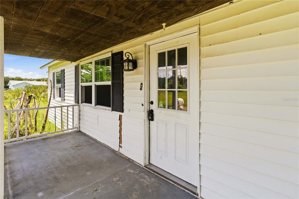A covered porch with white siding, a glass-paneled door, and a concrete floor — 2994 BIG SKY BOULEVARD, KISSIMMEE, FL