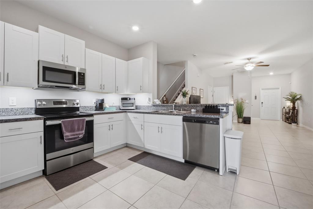 A kitchen with white cabinets, stainless steel appliances, and granite countertops opens to a living area — 4459 GLOBE THISTLE DRIVE, TAMPA, FL