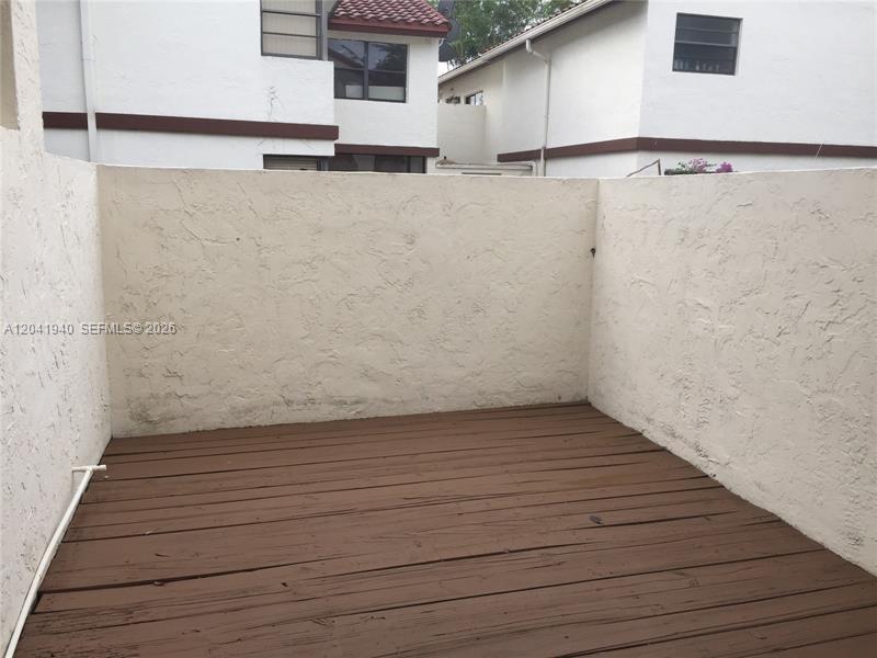 A small, enclosed wooden deck patio sits between two white stucco residential buildings — 331 Ives Dairy Rd # 10, Miami FL 33179, MIAMI, FL